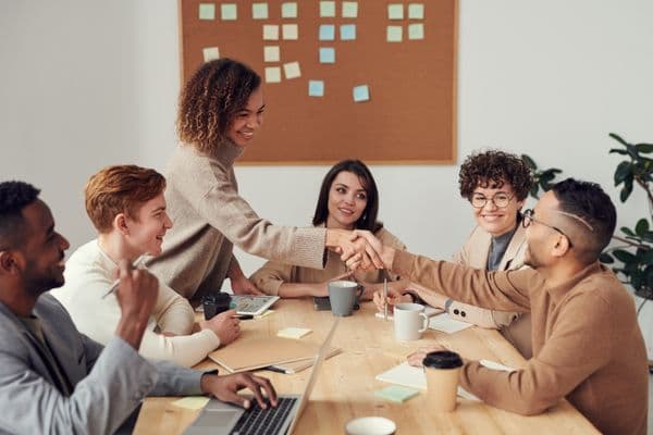 Imagine a hopeful entrepreneur of Black descent sitting in a bank, his business plan spread out before him as he explains his vision to a banking officer. The entrepreneur is wearing a smart-casual outfit and the banking officer, a South Asian woman, is attentively listening, her corporate attire bespeaking her position. The spacious room is filled with the calm ambiance of a professional setting, decorated with minimalist furniture, well-lit and with a large window overlooking the city skyline.